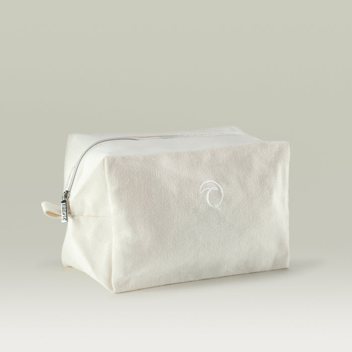 A minimalist beige Tropic toiletry bag made from fabric, featuring a subtle embroidered Tropic logo, silver zipper, and simple rectangular shape, displayed against a neutral background.