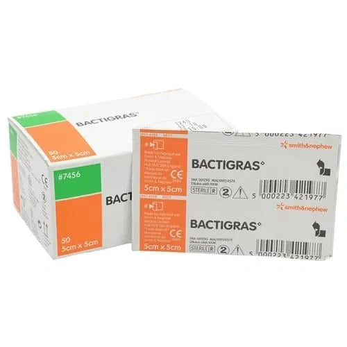 A box and packet of BACTIGRAS 5cm x 5cm sterile dressings sit on a surface. The box contains 50 dressings; the packet shows product details, including #7456, and Smith & Nephew branding.