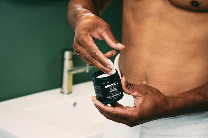 Man applying Brickell shave butter to hand in bathroom near sink.