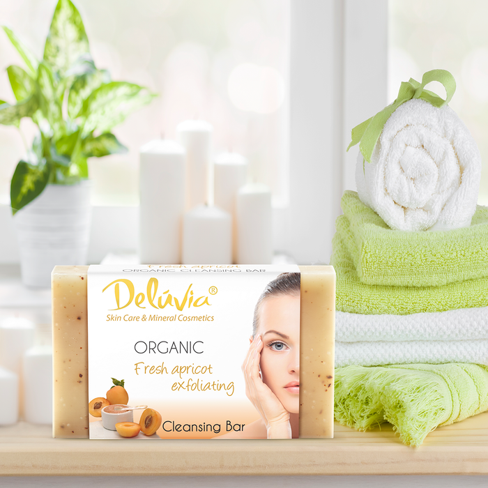 A bar of Deluvia soap on a bathroom counter with towels and a plant.