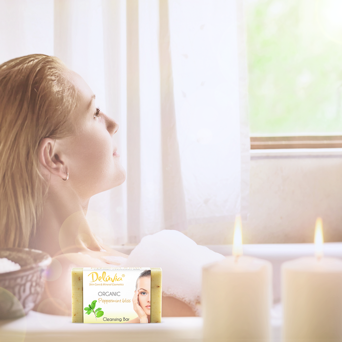 A woman in a bubble bath with candles and a bar of Deluvia soap.