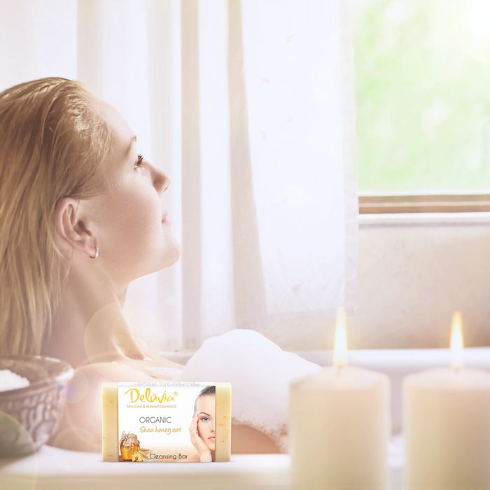 A woman in a bubble bath with candles and a bar of Deluvia soap.
