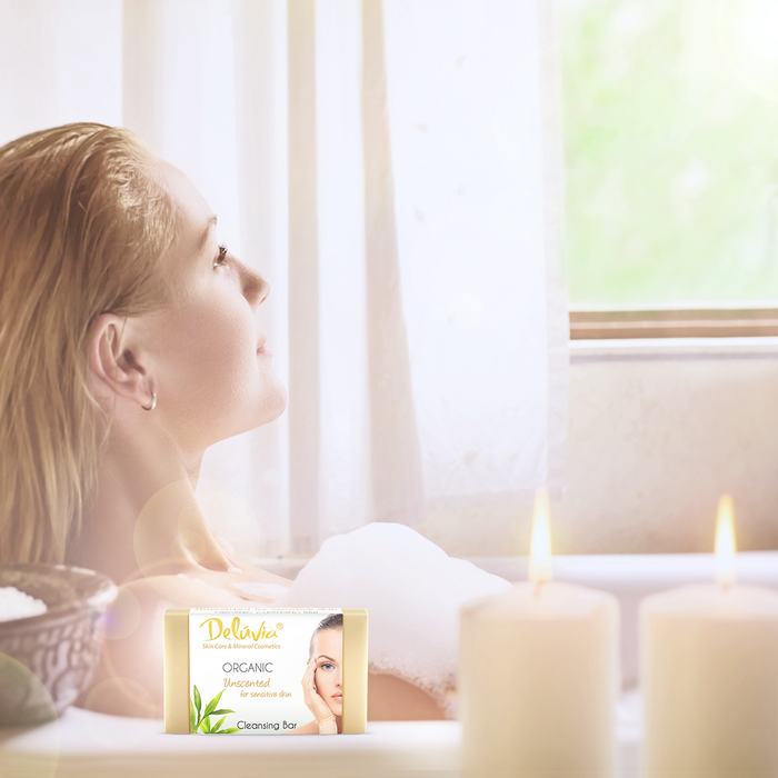 A woman in a bubble bath with candles and a bar of Deluvia Soap