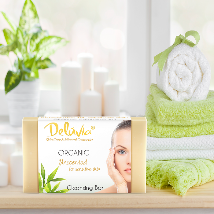 A bar of Deluvia soap on a bathroom counter with towels and a plant.