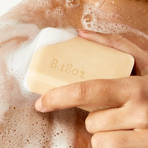 An image of a model rubbing the sudsy Sunshine Lemon 3.5 oz bar soap onto her shoulder.