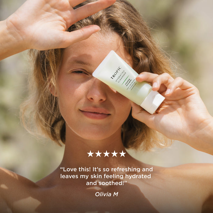 Person holding Tropic Hydrating Cleanser beside their face with five-star customer review: "Love this! It's so refreshing and leaves my skin feeling hydrated and soothed!" – Olivia M.