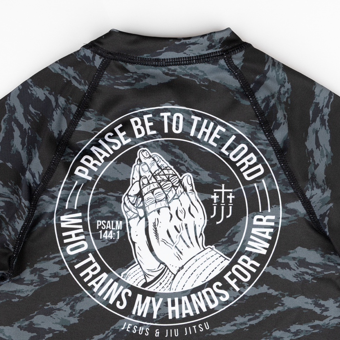 Black and gray camouflage rash guard with praying hands graphic and text on a white background