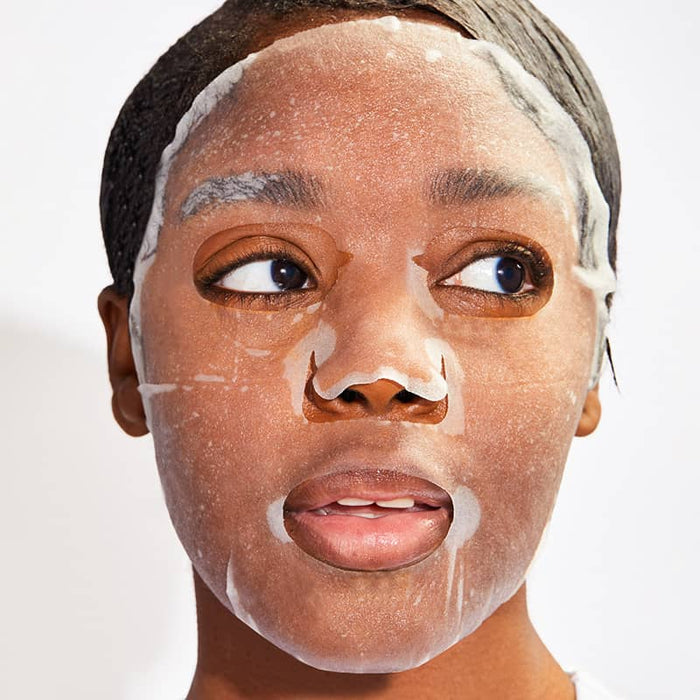 Woman wearing a foaming sheet mask with visible bubbles, looking to the side, highlighting an active cleansing or oxygenating skincare treatment for refreshed, purified skin